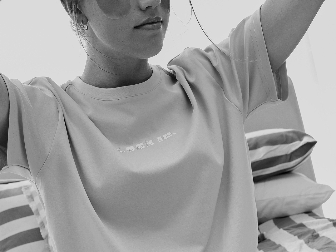 A woman taking a selfie with her arms raised, wearing sunglasses and a T-shirt, in black and white.