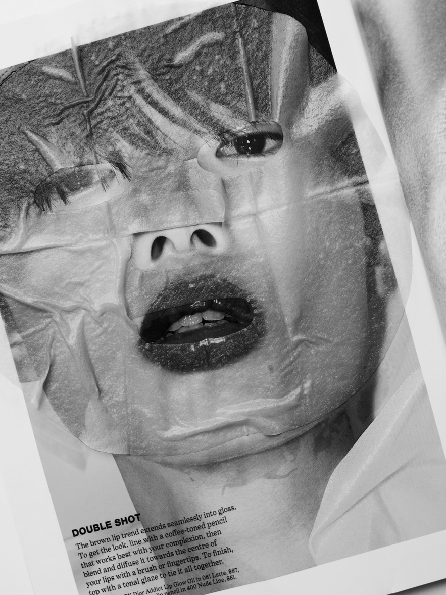 Black and white photograph of a torn print featuring a close-up of a person's face with eyes closed, mouth slightly open, and a mask or overlay covering part of the face. There is visible text at the bottom mentioning makeup application instructions.