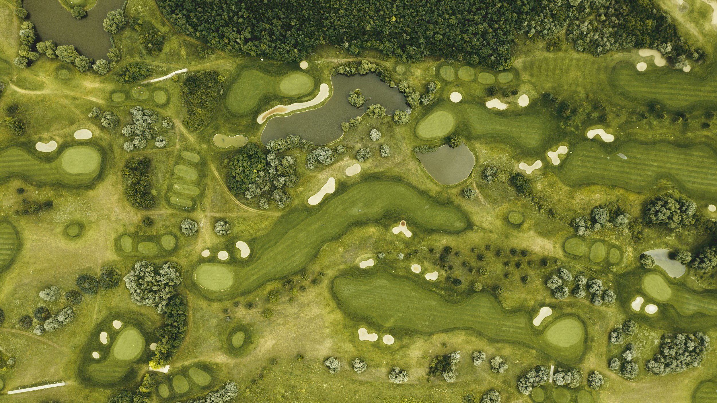 Aerial view of a golf course with multiple fairways, greens, and sand bunkers, surrounded by trees and water hazards.