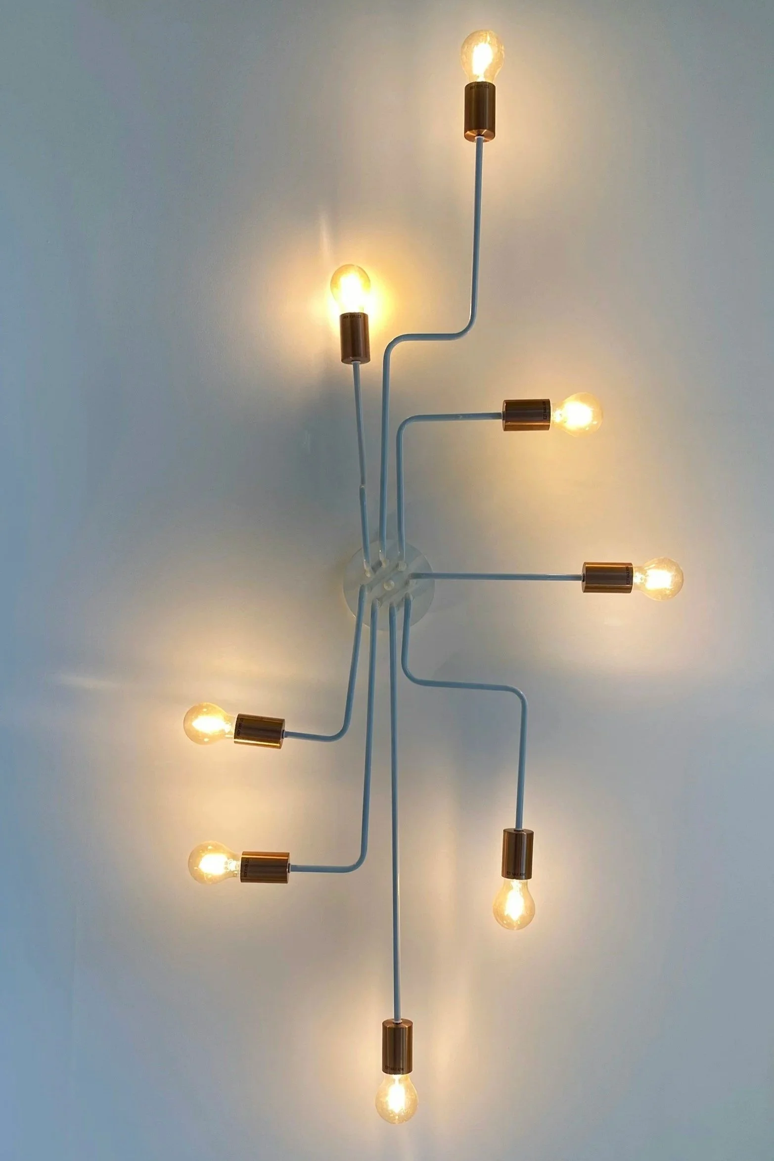 Modern ceiling light fixture with multiple exposed illuminated bulbs connected by curved white metal arms and gold-colored fittings.