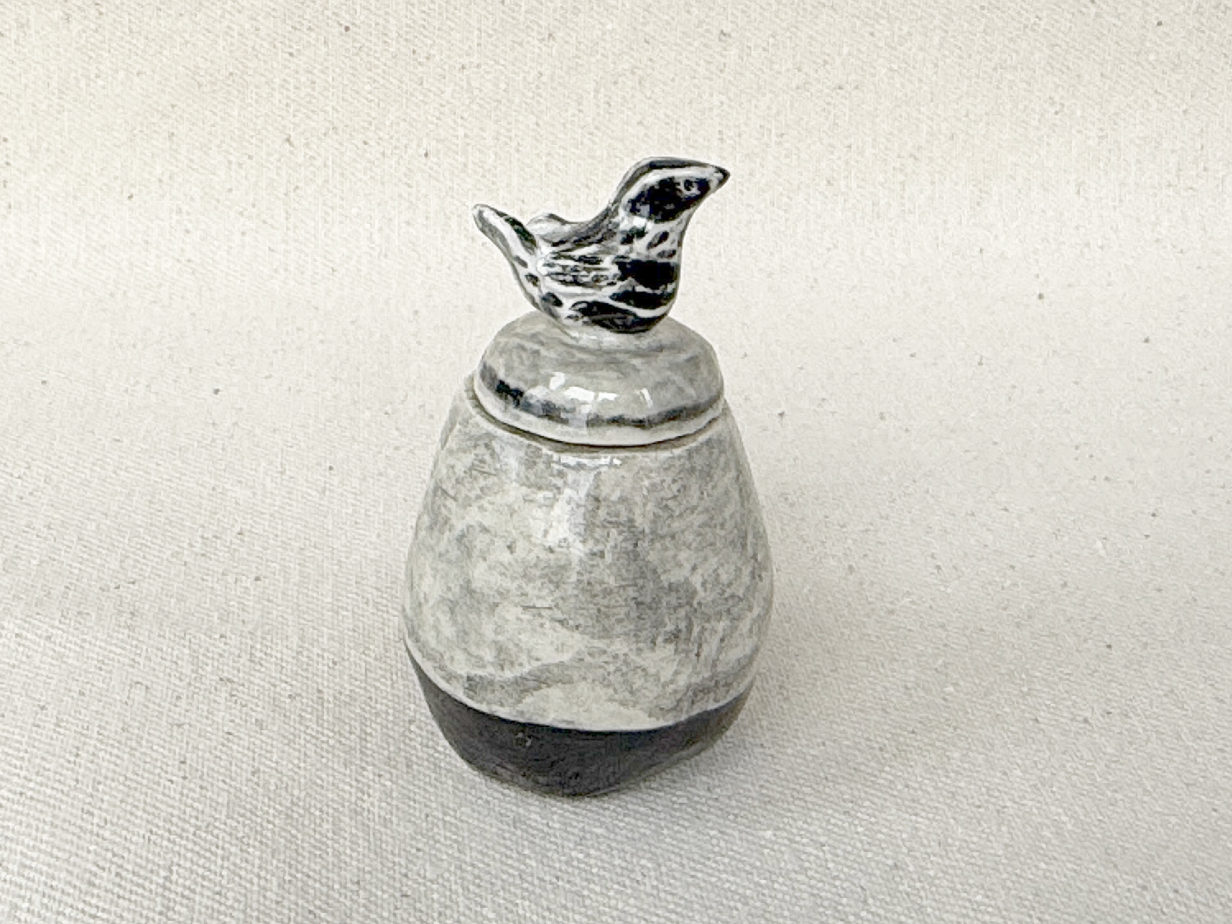 A small metallic bird figurine on top of a stone or ceramic container.