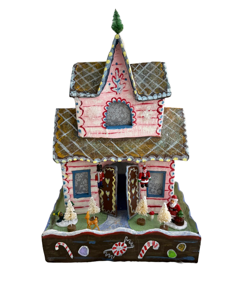 Gingerbread house decorated with icing, candy, and small figurines including Santa Claus, nutcracker soldiers, and a reindeer, with snow and trees display at the base.
