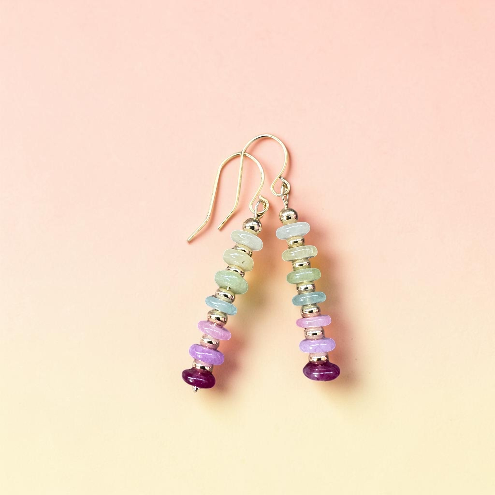 A close-up of pastel-colored earrings with beads, displayed against a pink and cream background.