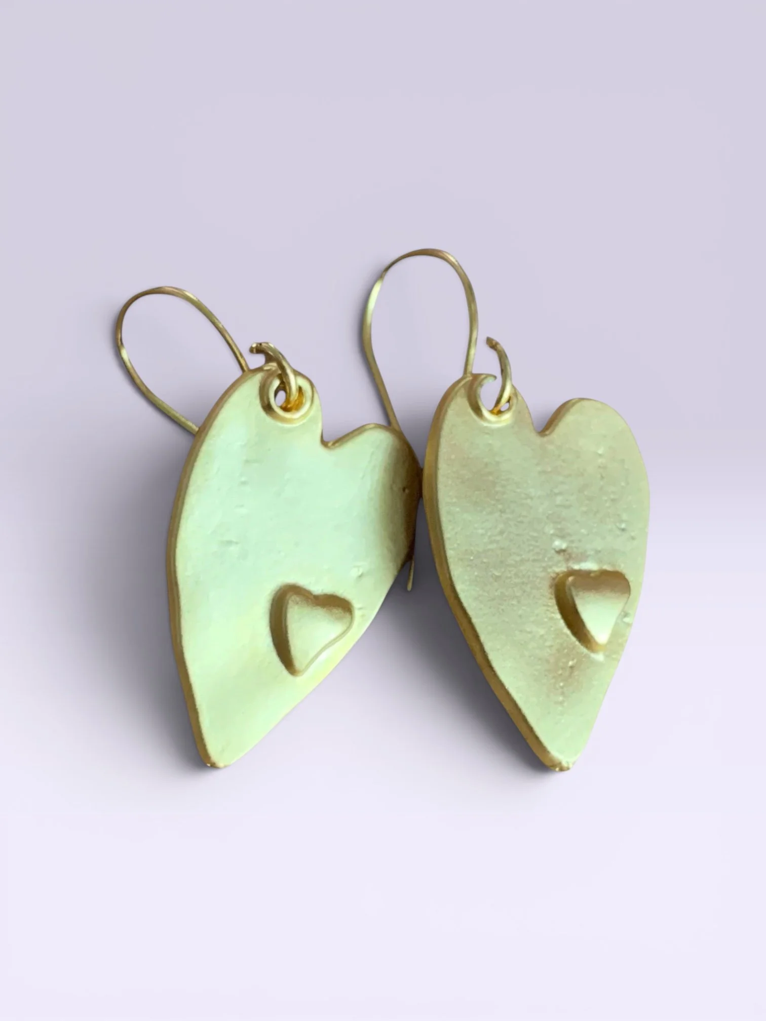 Pair of gold-colored earrings shaped like dog faces with heart-shaped nose holes, against a light purple background.