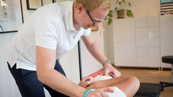 A healthcare professional performs a physical exam on a patient's leg in a clinical setting.