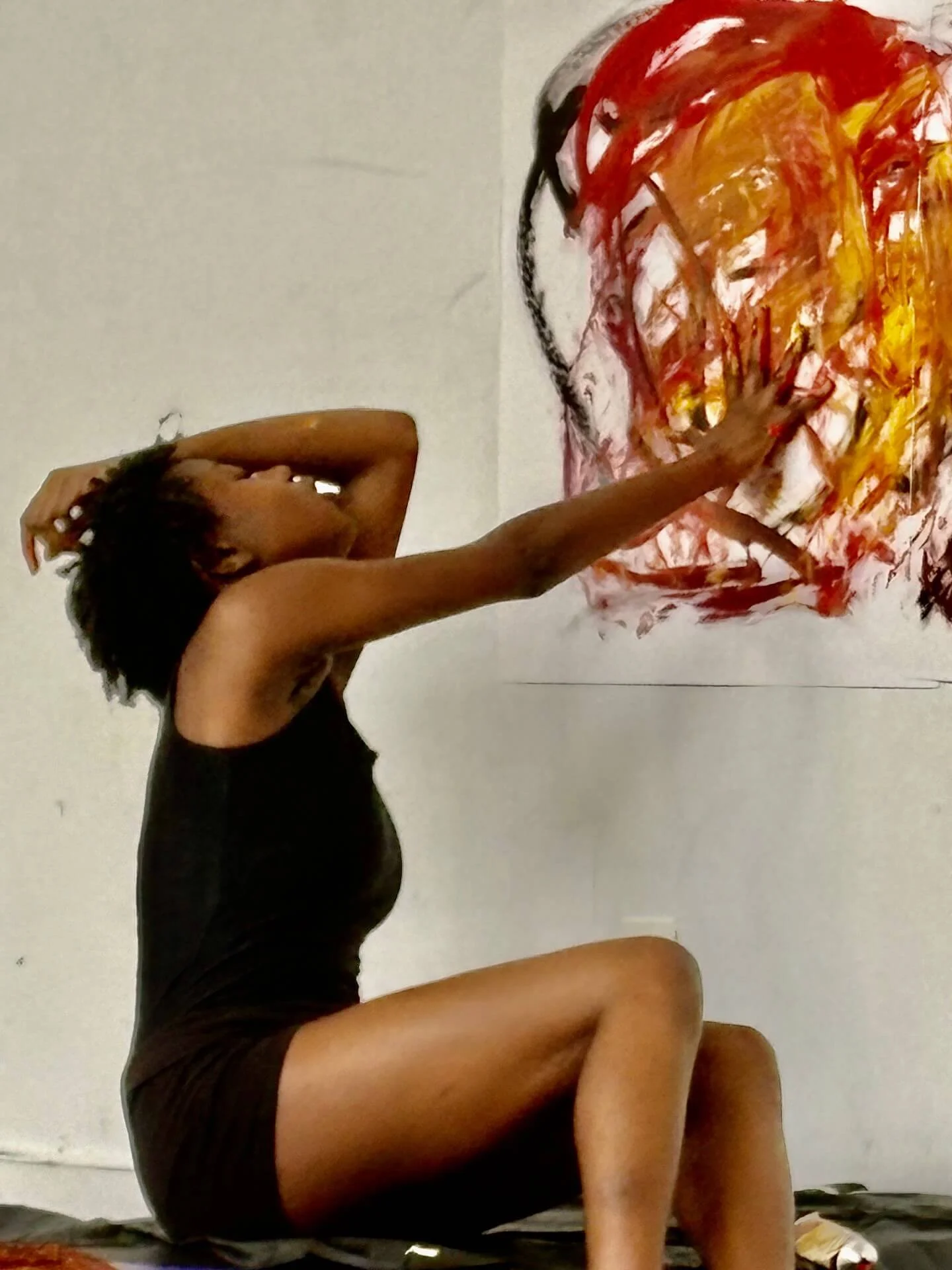 A woman wearing a black sleeveless dress creates a colorful abstract painting with her hands on a white wall as part of a movement exercise.