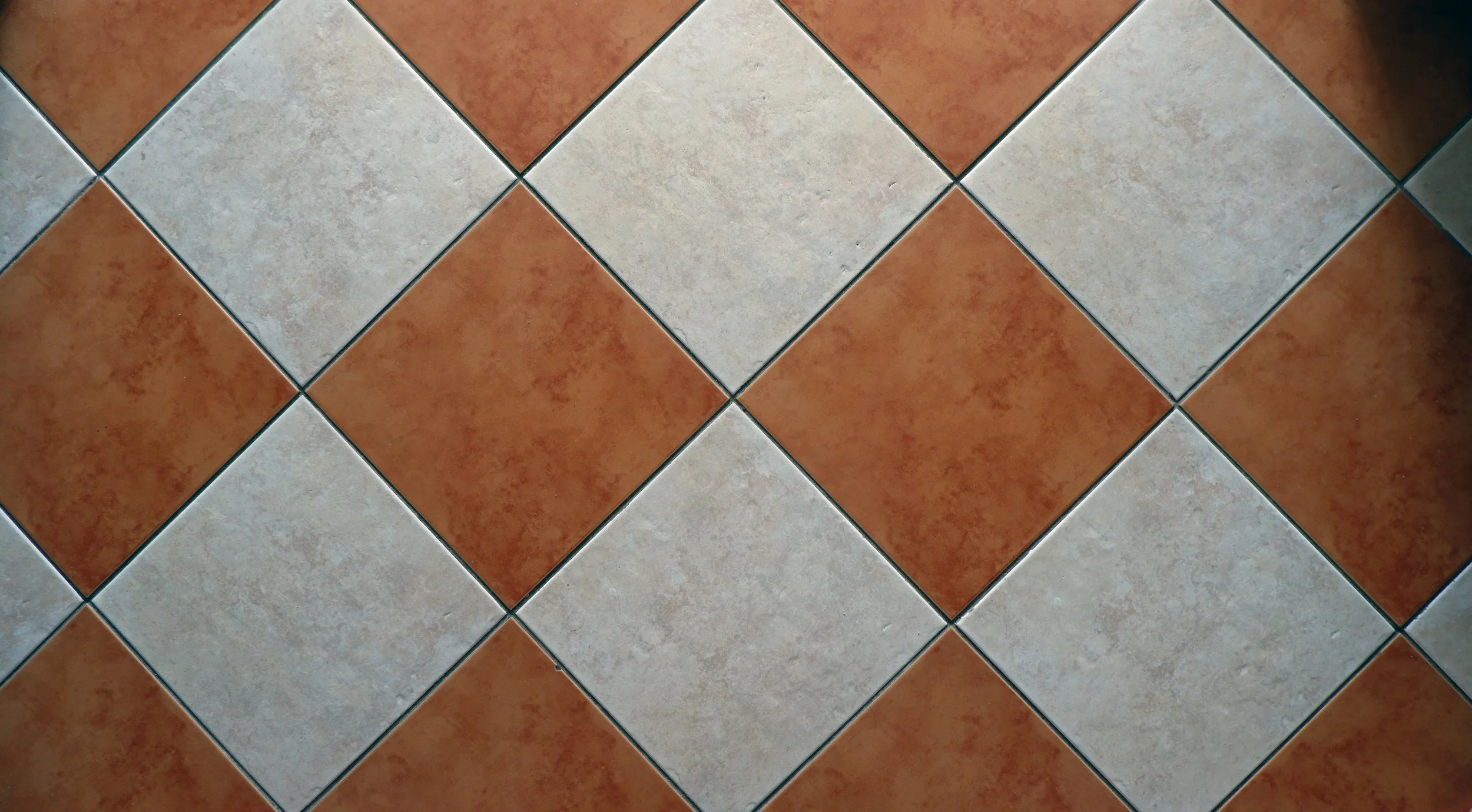 A tiled floor with a repeating pattern of alternating reddish-brown and beige tiles, arranged in a diagonal checkerboard layout.