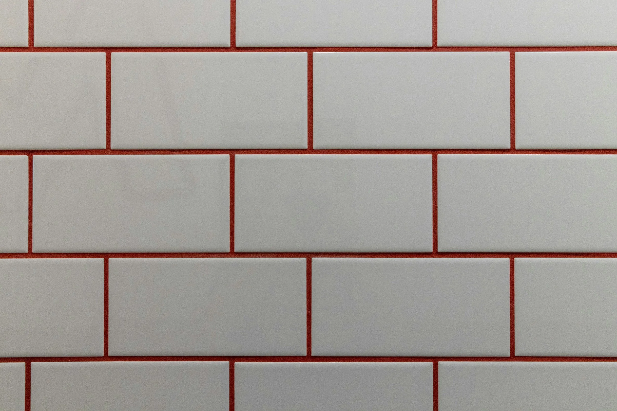 A close-up view of a wall with white rectangular tiles and red grout lines.