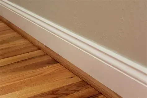 Close-up of a baseboard and hardwood flooring, with a beige wall.
