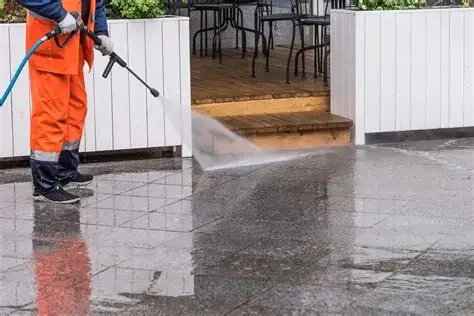 Person using a pressure washer to clean a concrete patio outside a house.