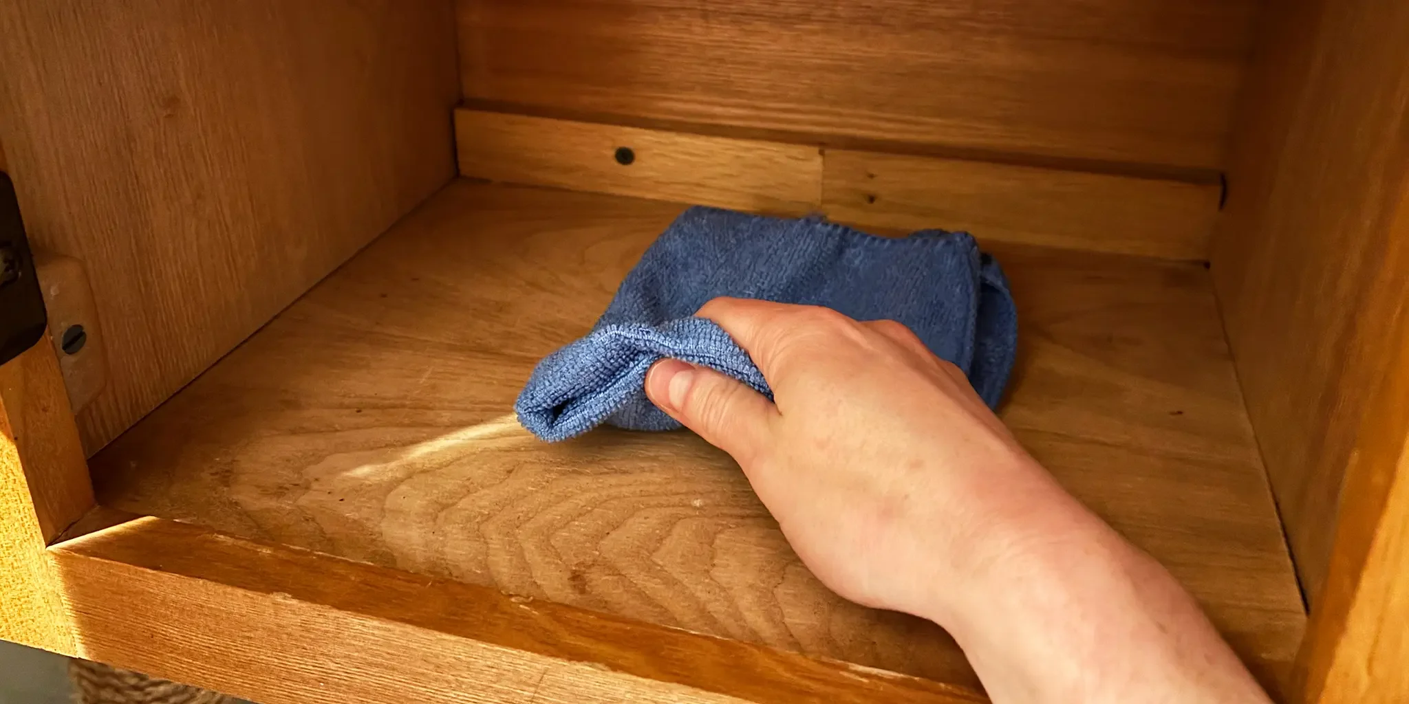 Hand cleaning the inside of a wooden drawer with a blue cloth.