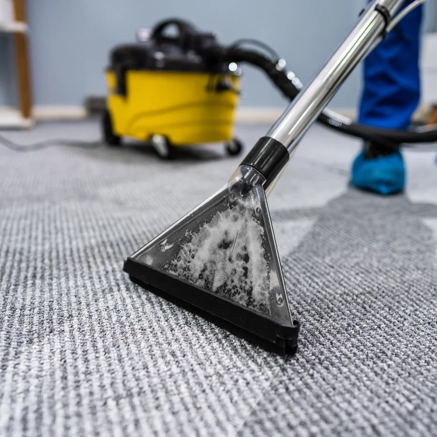 A person cleaning carpet with a steam cleaning machine in a room.