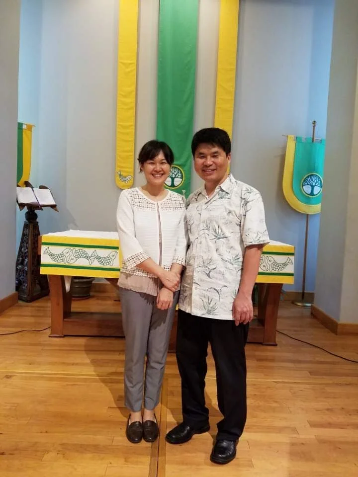 두 사람이 교회 내부에서 함께 사진을 찍고 있으며, 배경에 십자가와 교회 깃발이 걸려 있음.