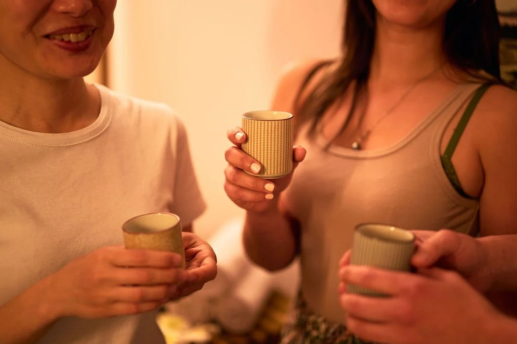 Trois personnes tiennent des tasses lors d'une rencontre informelle dans un intérieur chaleureux.