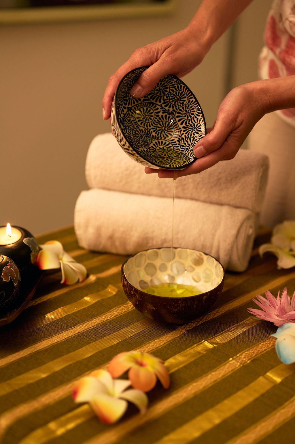 Une personne verse de l'huile dans un bol décoratif sur une table avec des fleurs et des bougies