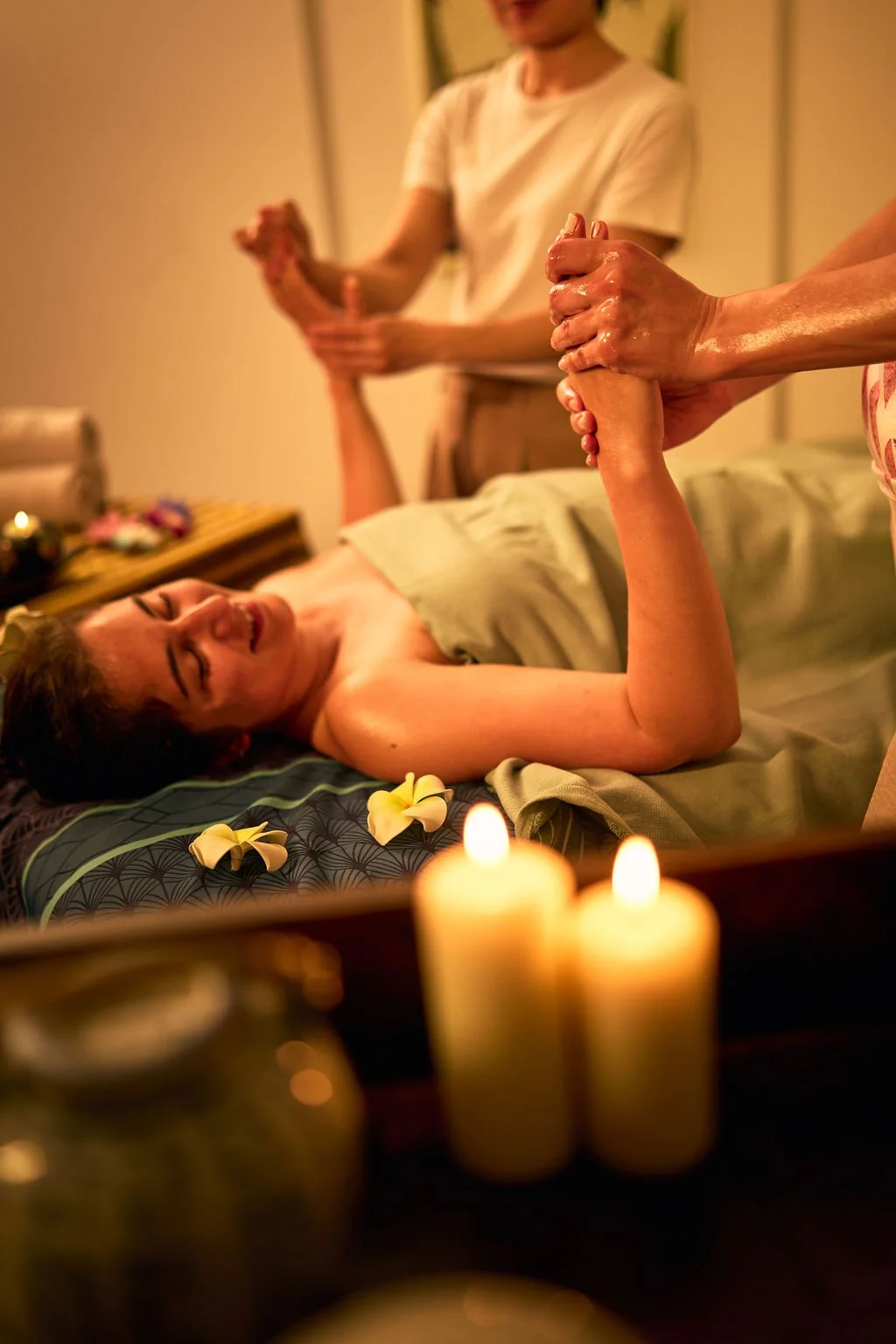 Une femme souriante reçoit un massage relaxant dans une ambiance tamisée avec des bougies et des fleurs