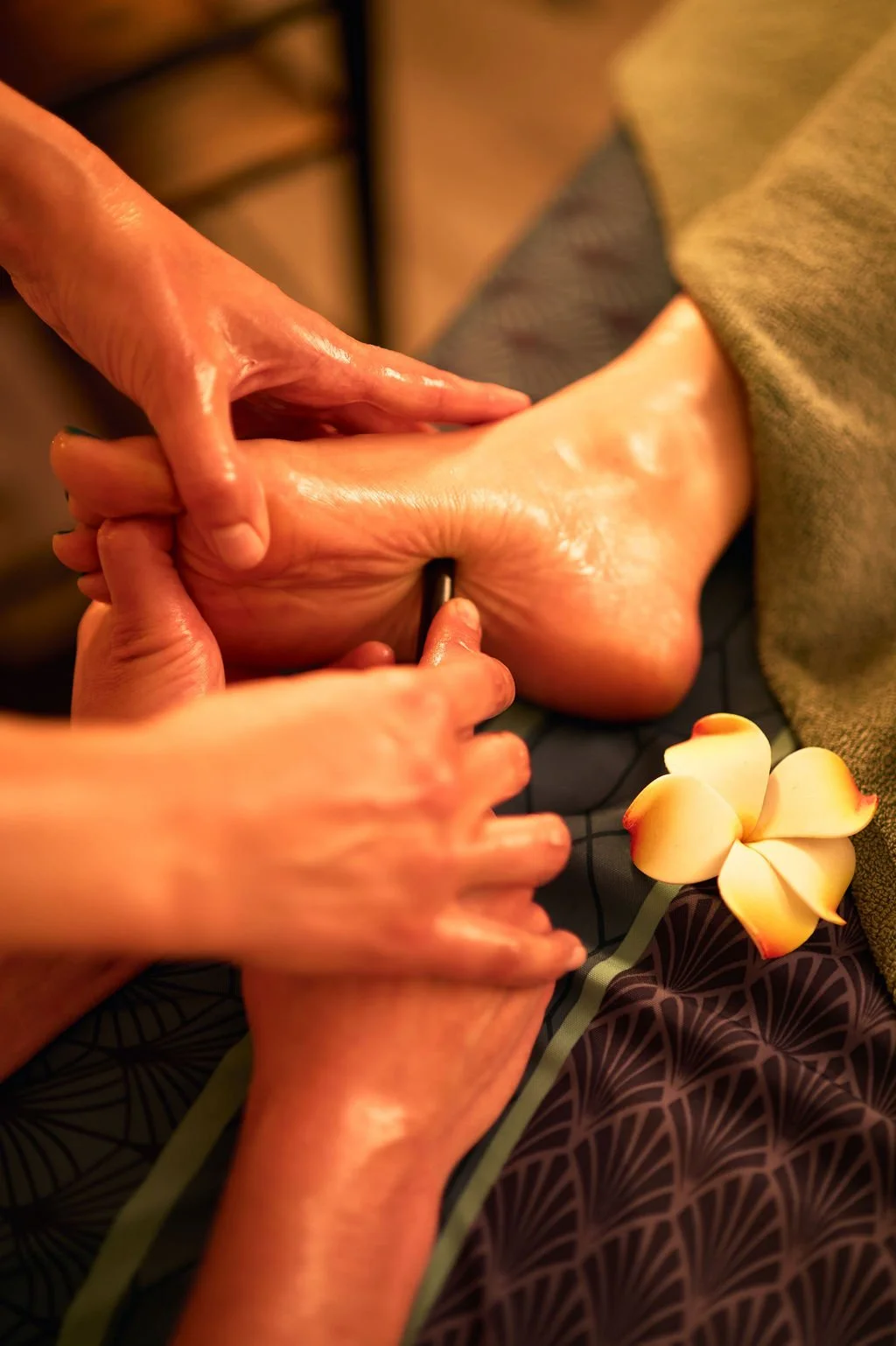 Une personne reçoit un massage des pieds par une autre personne dans un cadre relaxant, avec des fleurs blanches à proximité.