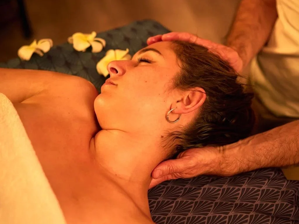 Une femme reçoit un massage relaxant dans un spa, allongée sur une table avec des fleurs jaunes autour d'elle.