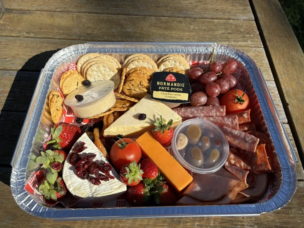 Charcuterie tray with cheese, crackers, grapes, strawberries, tomato, cured meats, dip, and olives.