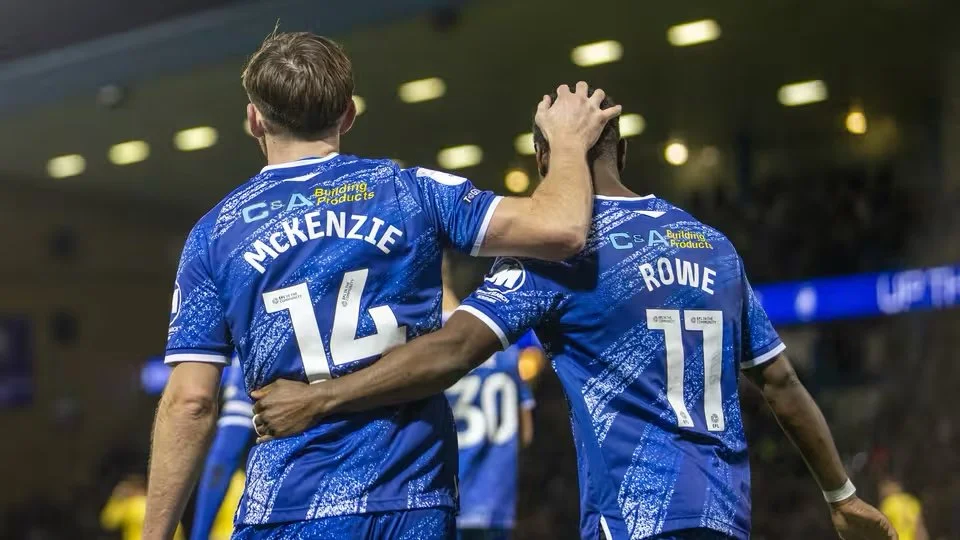 Two soccer players in blue uniforms celebrating on the field, with one player patting the other's head.