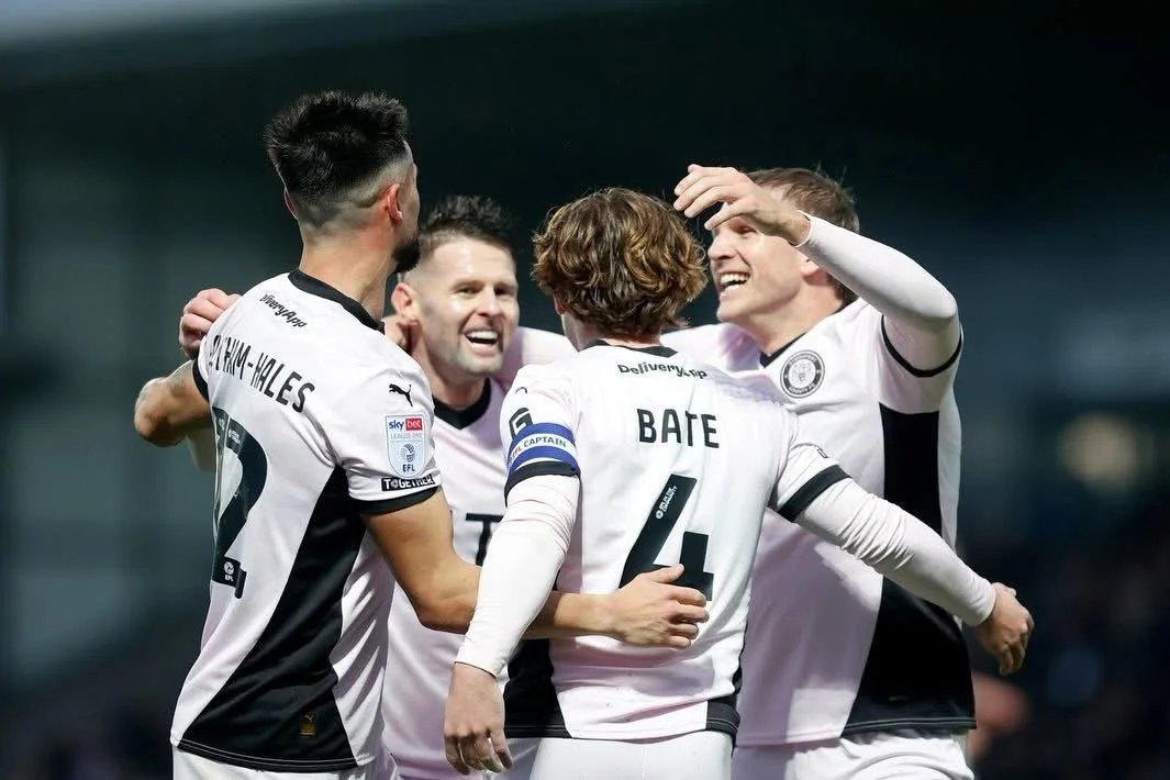 Soccer players in black and white uniforms celebrating on the field, smiling and hugging.