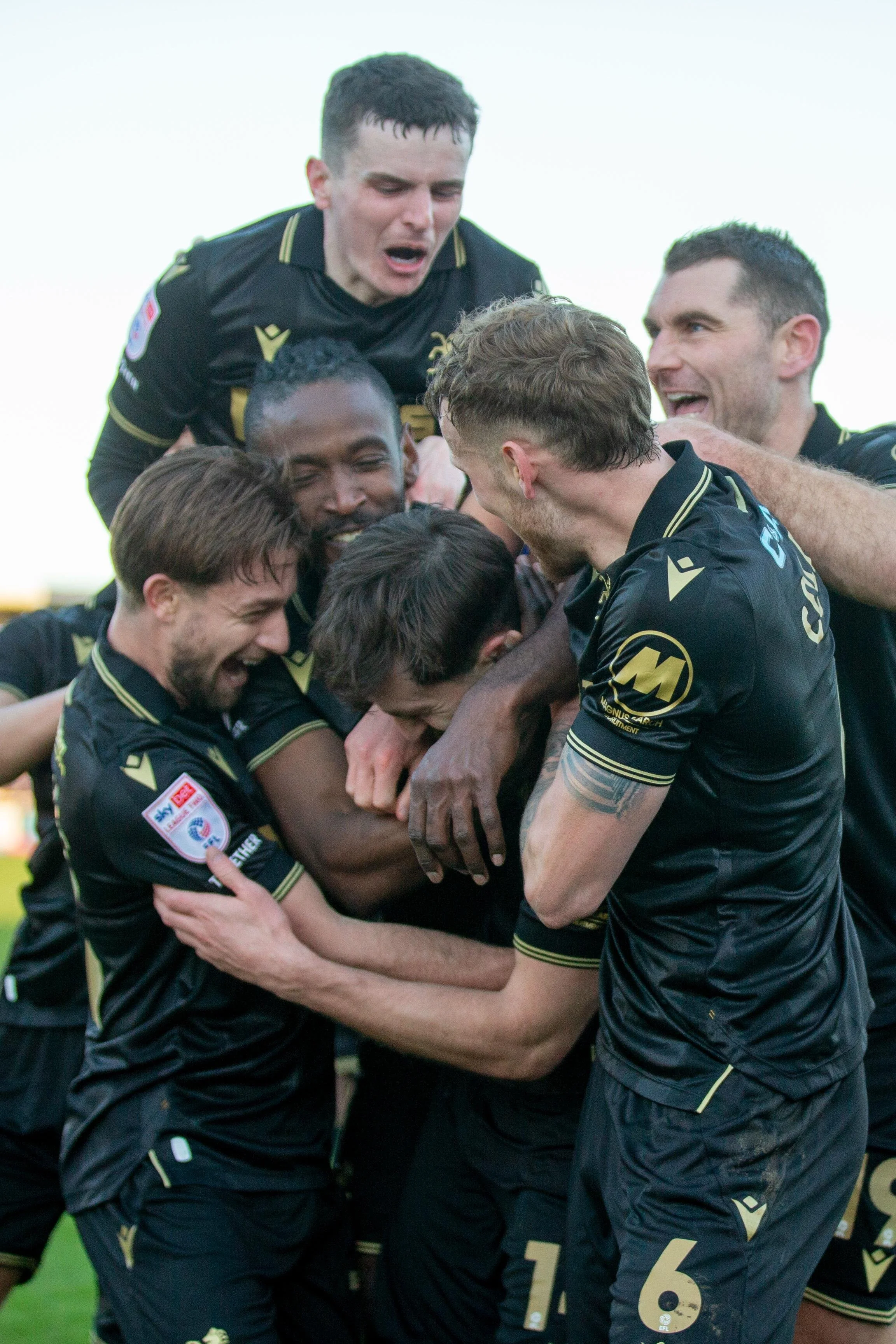 A group of soccer players in black and gold uniforms celebrating together on the field.