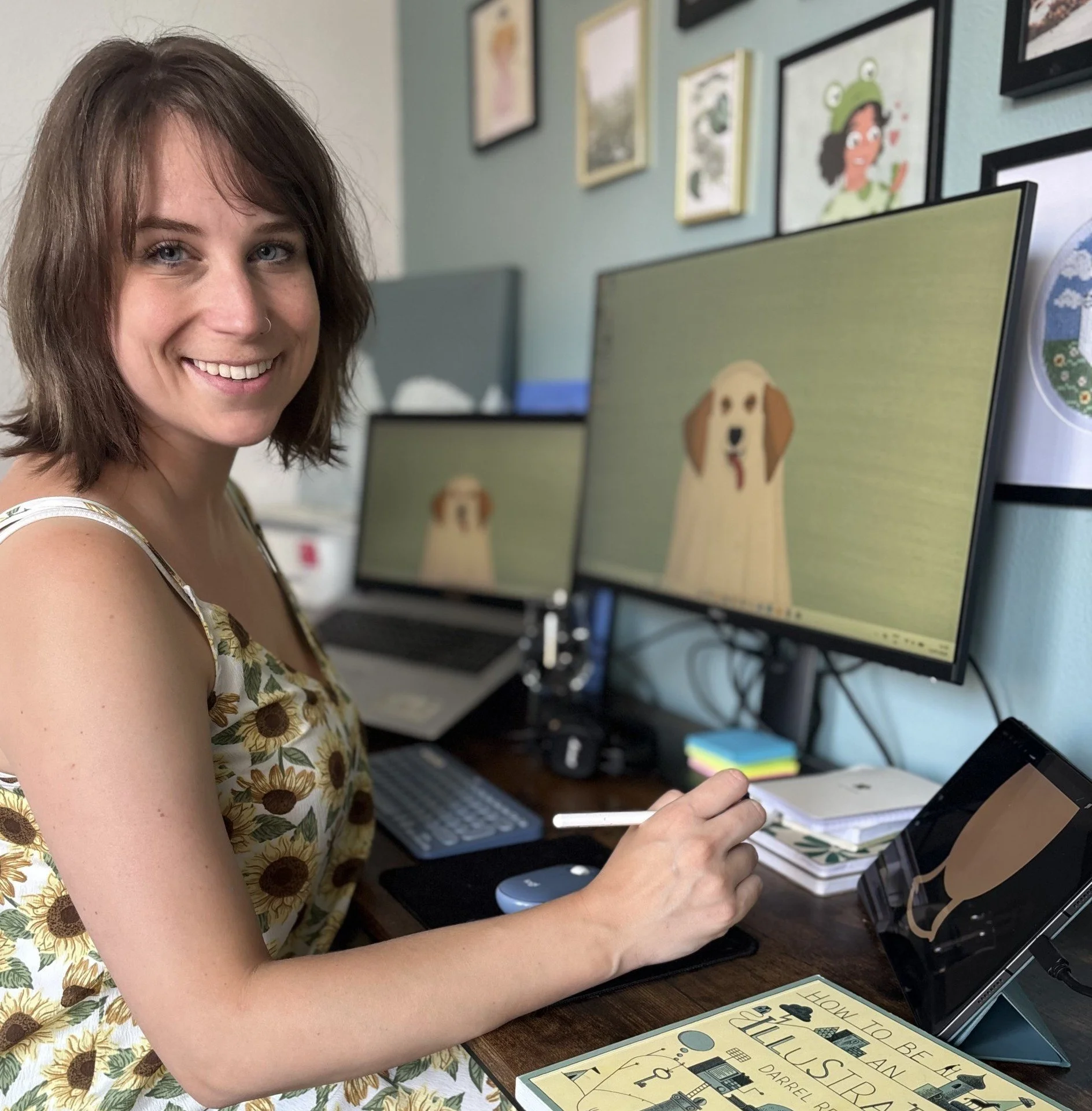 Photo of illustrator Sammy Godding at her desk, smiling at the camera
