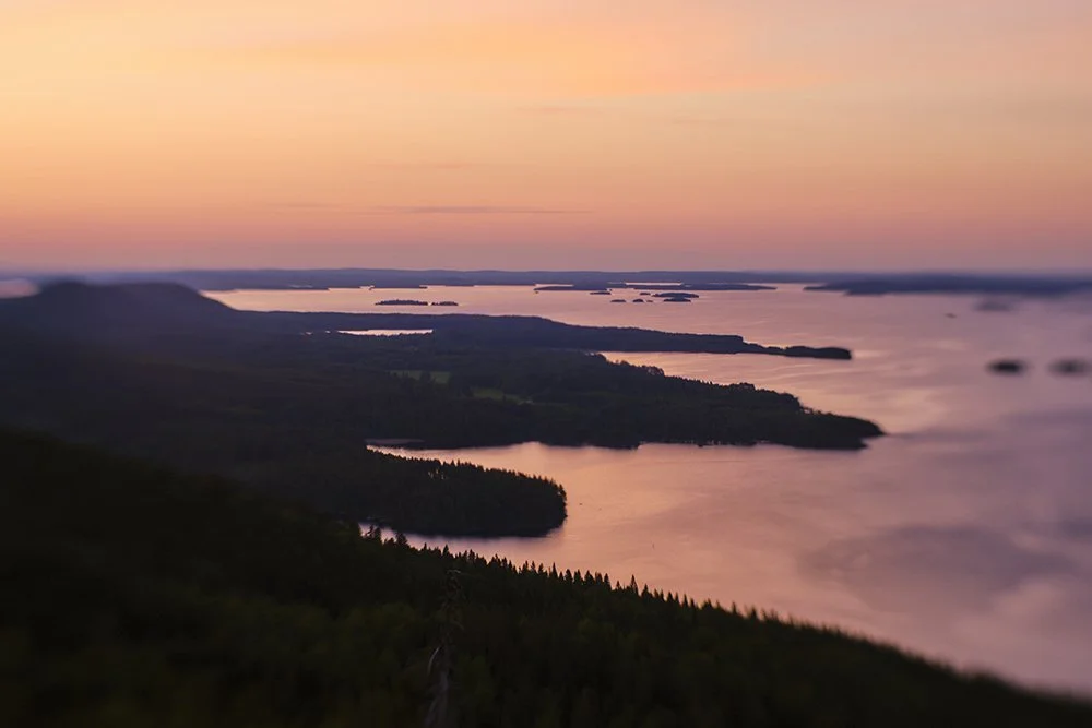 A scenic view of a large body of water with islands and landmasses at sunset, with a colorful sky and distant horizon.