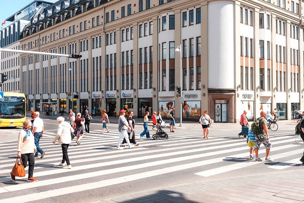 People crossing the street at a busy crosswalk in front of a multi-story building with retail stores.