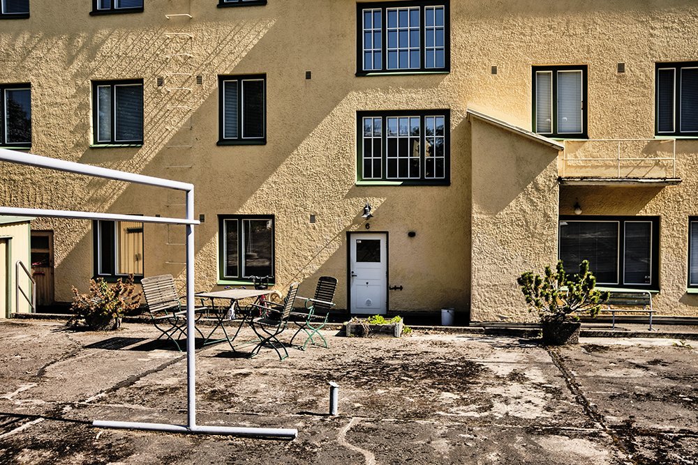 Backyard patio with a yellow stucco apartment building, outdoor furniture, potted plants, and a clothesline.