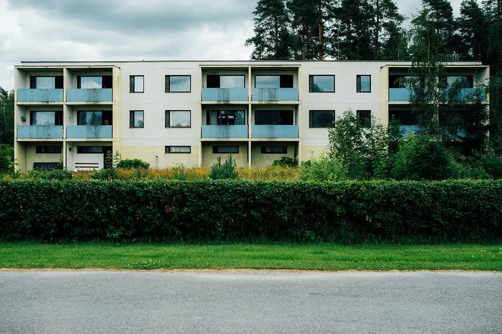 A multi-story apartment building with balconies, surrounded by greenery and trees.