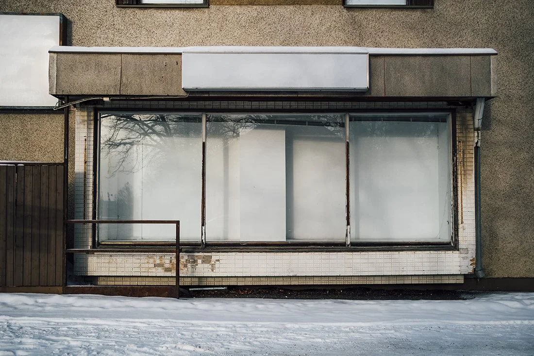Harmaa rakennus, jossa on suuri ikkunaruutu peitelevyllä, ja lunta maassa edessä.