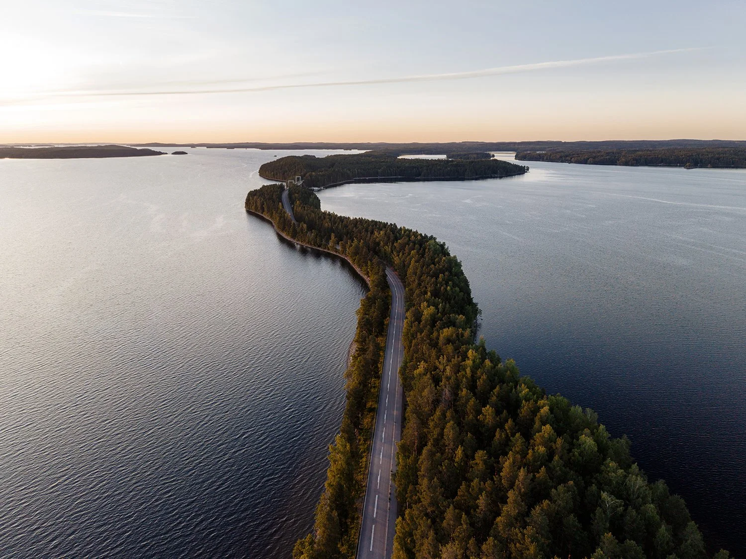 Lentokoneen näkymä järven ja metsän peittämän niemimaan yli auringon lounastaessa taivaalla.