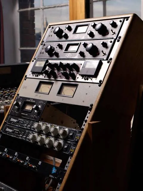 A collection of audio equipment, including vintage and modern audio processors, tuners, and controllers, mounted on a wooden stand.