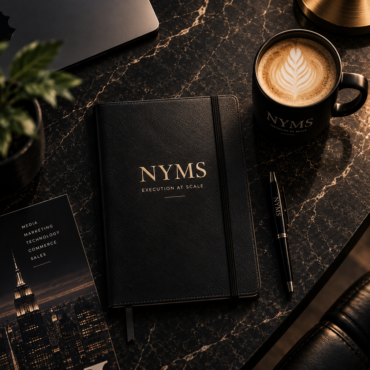 A black notebook with "NYMS Execution at Scale" written on the cover, a pen with the same branding, a coffee mug with latte art and branding, a potted plant, and a brochure with cityscape at night on a dark marble desk.