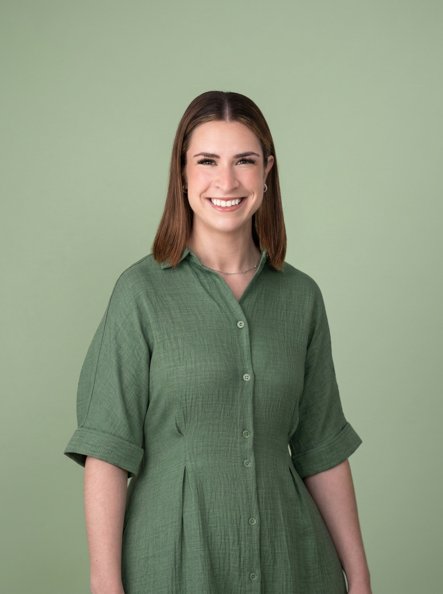 A smiling woman with shoulder-length brown hair wearing a green button-up dress standing against a light green background.
