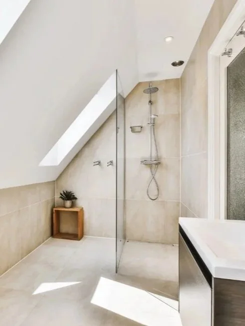 Aménagement d’une salle de bain mansardée avec douche à l’italienne, carrelage clair et meuble vasque, pour exploiter au mieux un espace sous pente.