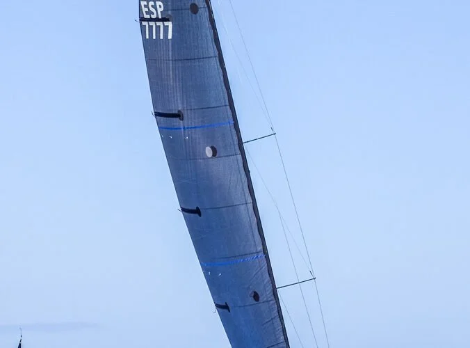 Velero de competición con vela azul marino y marcado con código ESP 7777 en un día despejado.