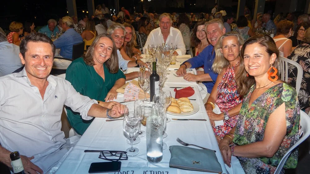 Grupo de personas sonriendo sentado en una mesa durante una comida o evento social en un lugar cerrado