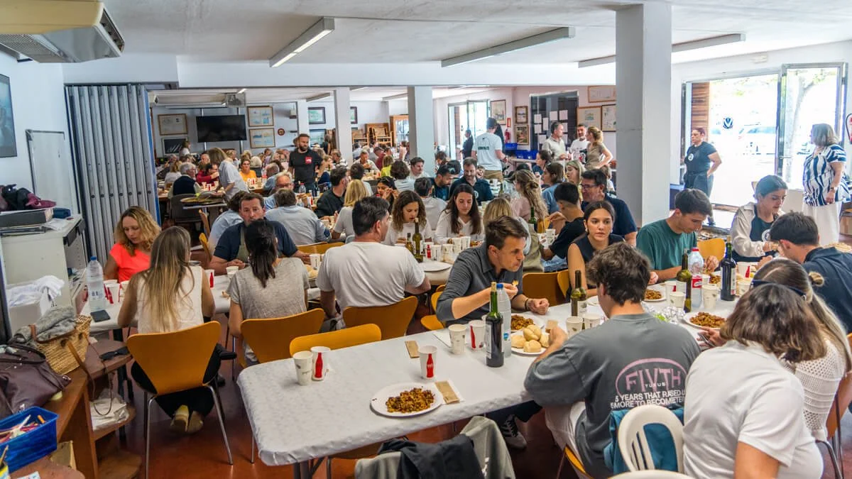 Personas comiendo en un comedor, muchas mesas llenas, ambiente concurrido con comida y bebidas