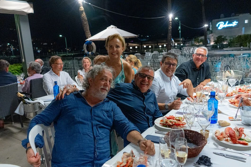 Grupo de personas en una cena al aire libre, disfrutando de mariscos y vino, en una noche con ambiente relajado y decoraciones contemporáneas.