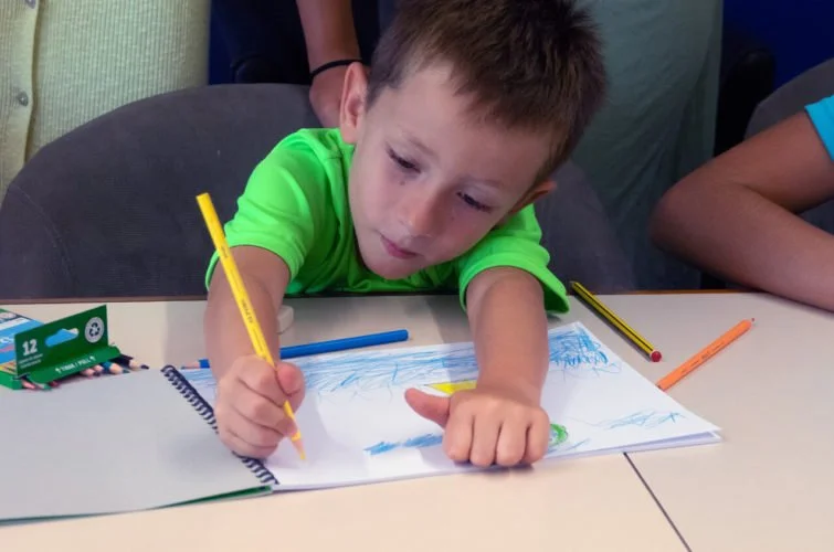 Niño dibujando en una libreta en una mesa.