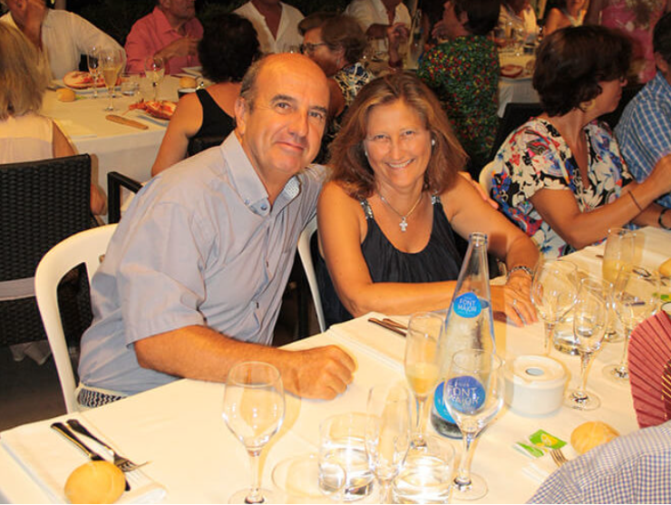 Pareja sonriendo en una cena con muchos comensales y comida en la mesa.