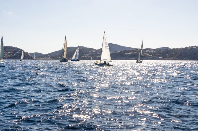 Varios barcos de vela navegando en un cuerpo de agua con colinas al fondo.