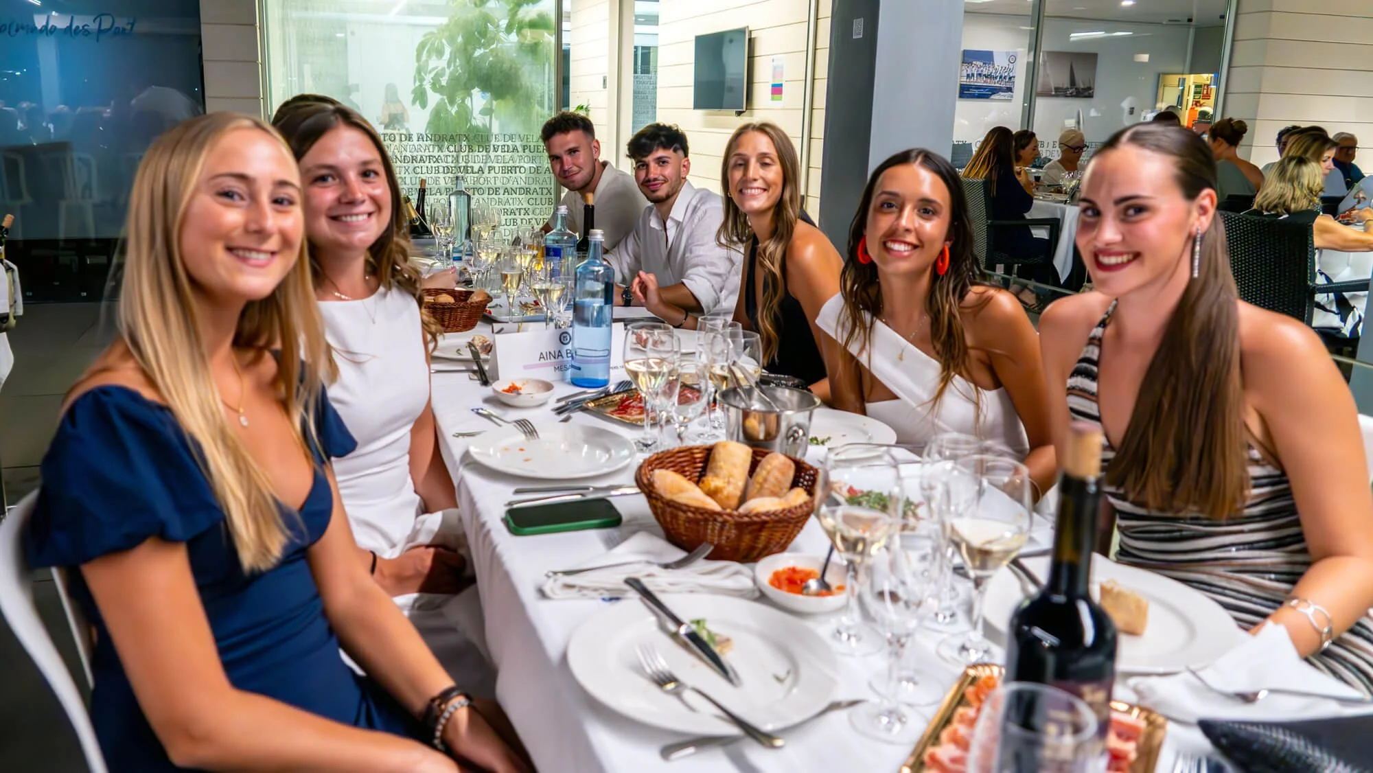 Grupo de personas jovenes sonriendo y disfrutando en una cena en un restaurante, con comida y bebidas sobre una mesa.