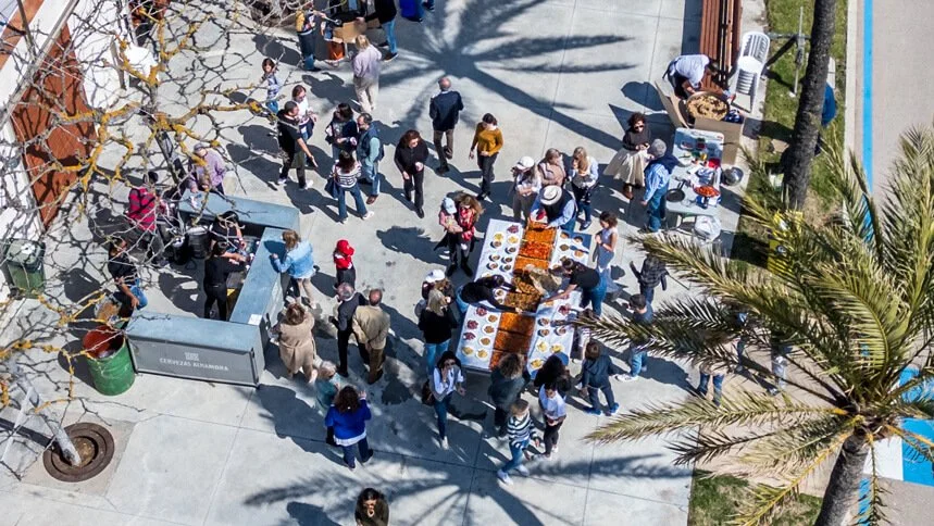 Personas en una feria de comida o mercado al aire libre, con puestos de comida y gente comprando y socializando.