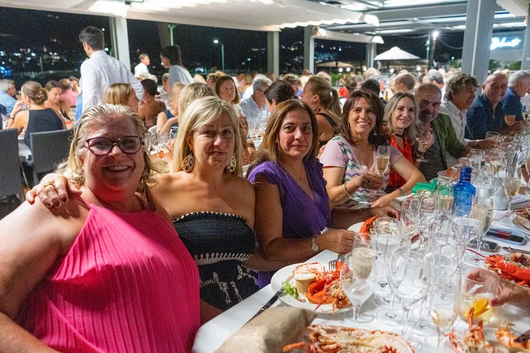 Grupo de personas sentadas en una mesa en un banquete o celebración, con comida y bebidas en un ambiente nocturno.