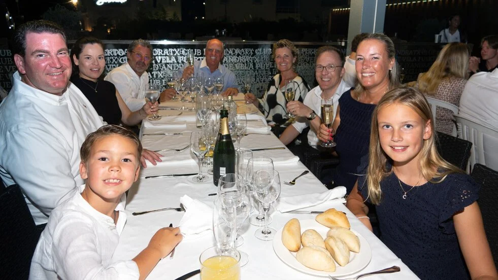 Grupo de personas reunidas en cena elegante en un restaurante, con comida y bebida en la mesa.