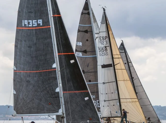 Tres veleros de regata navegando en el agua con cielo nublado.