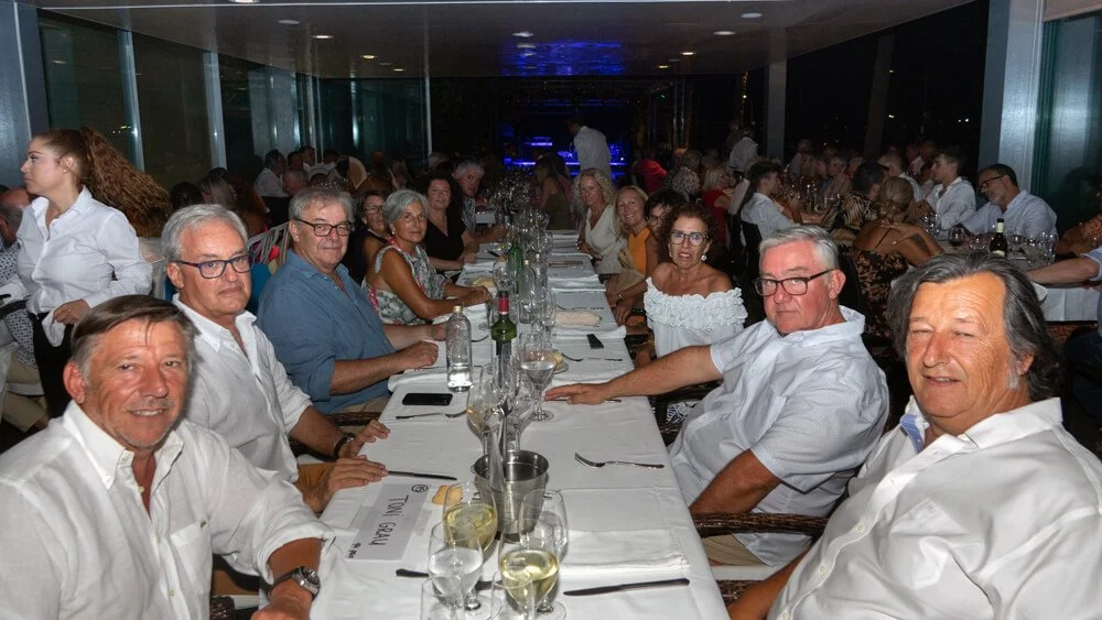Personas sentadas en una mesa larga en un restaurante, celebrando una comida o reunión social, con varios platos y bebidas.
